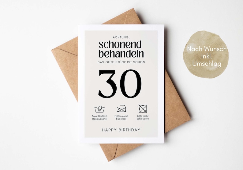 May include: A white card with black text that reads "ACHTUNG, schonend behandeln DAS GUTE STUCK IST SCHON 30" with three black and white icons below the text. The icons represent washing instructions. The text "HAPPY BIRTHDAY" is below the icons. The card is sitting on a brown envelope.