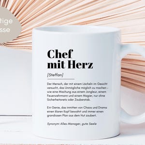 May include: White ceramic mug with a black design that reads "Chef mit Herz [Steffan]" and a definition of the term in German. The mug has a black handle.