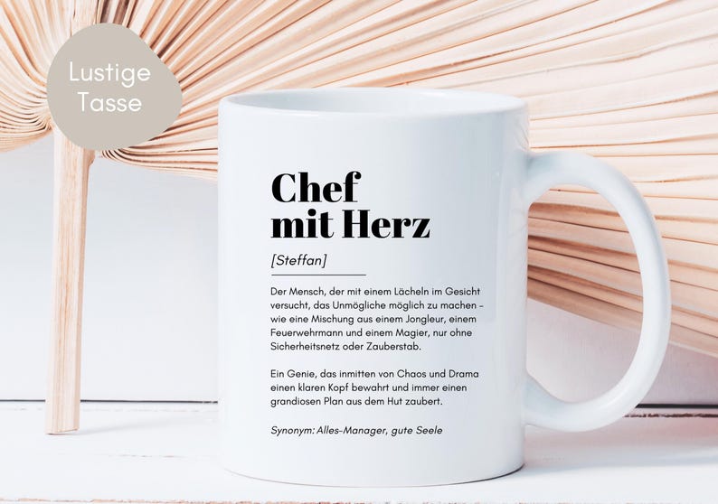 May include: White ceramic mug with a black design that reads "Chef mit Herz [Steffan]" and a definition of the term in German. The mug has a black handle.
