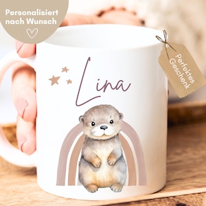 May include: White ceramic mug featuring a watercolor illustration of an otter, a rainbow, and the name "Lina" in cursive. The mug has a handle and a small tag that says "Perfect Gift". The mug is personalized with the text "Personalized on request".