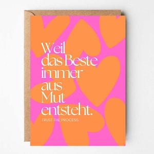 Könnte beinhalten: Eine Grußkarte mit pinkfarbenem Hintergrund und orangefarbenen Herzformen. Der deutsche Text "Weil das Beste immer aus Mut entsteht. Trust the process" ist in Weiß geschrieben. Die Karte befindet sich in einem braunen Umschlag.