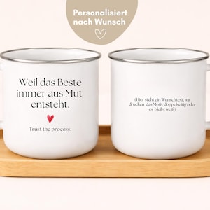 Può includere: Due tazze smaltate bianche con bordi argentati su un vassoio di legno. Una tazza ha il testo "Weil das Beste immer aus Mut entsteht" e "Trust the process" con un cuore rosso. L'altra tazza ha testo in tedesco. Le tazze sono personalizzate.