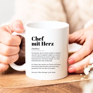 May include: White ceramic mug with a black inscription that reads "Chef mit Herz [Steffan]" and a definition of the term in German.
