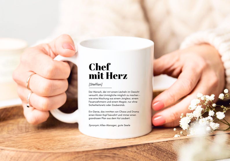 May include: White ceramic mug with a black inscription that reads "Chef mit Herz [Steffan]" and a definition of the term in German.