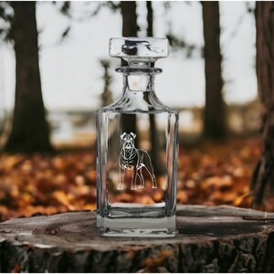 May include: A clear glass decanter with a square body and a stopper. The decanter features an etched design of a Boxer dog.