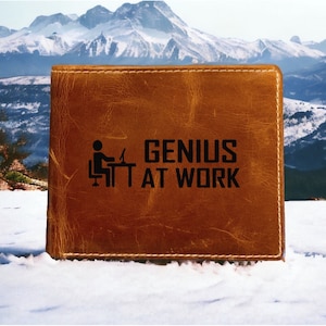 May include: A brown leather wallet with the text "GENIUS AT WORK" and a small icon of a person sitting at a computer.