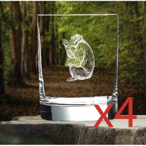 May include: Set of four clear glass tumblers with an etched design of a monkey. The tumblers are on a wooden surface.
