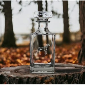 May include: A clear glass decanter with a square body and a stopper. The decanter features an etched design of a Dalmatian dog.