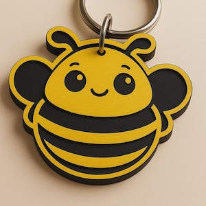 May include: A yellow and black bee-shaped keychain with a smiling face and a silver key ring.