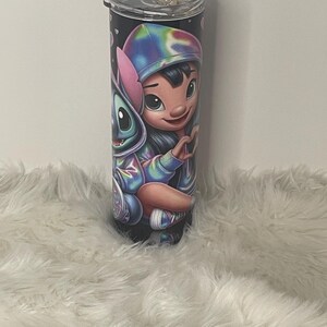 Puede incluir: Un vaso de acero inoxidable con tapa negra y una imagen colorida de Stitch y Lilo de la pel&iacute;cula Lilo & Stitch de Disney. La imagen presenta a Stitch con pelaje azul y a Lilo con una diadema rosa y una camisa azul y morada de te&ntilde;ido anudado.
