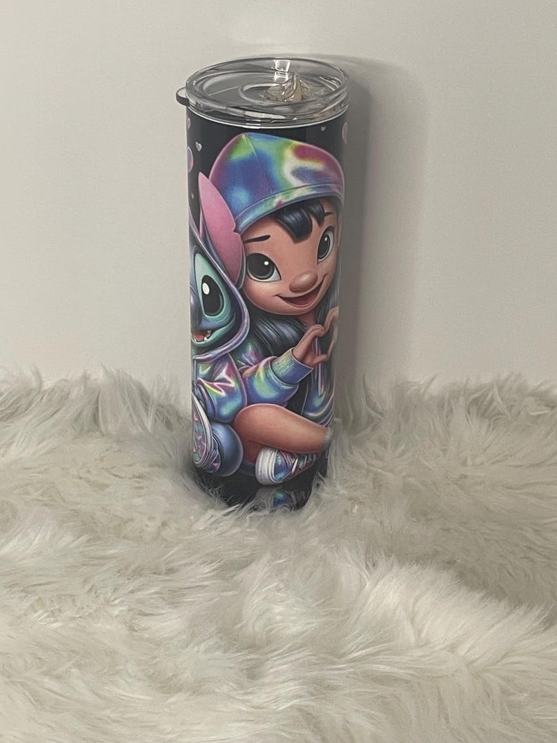Puede incluir: Un vaso de acero inoxidable con tapa negra y una imagen colorida de Stitch y Lilo de la pel&iacute;cula Lilo & Stitch de Disney. La imagen presenta a Stitch con pelaje azul y a Lilo con una diadema rosa y una camisa azul y morada de te&ntilde;ido anudado.