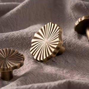 May include: Three gold-toned cabinet knobs with a sunburst design. The knobs are made of metal and have a smooth, polished finish.