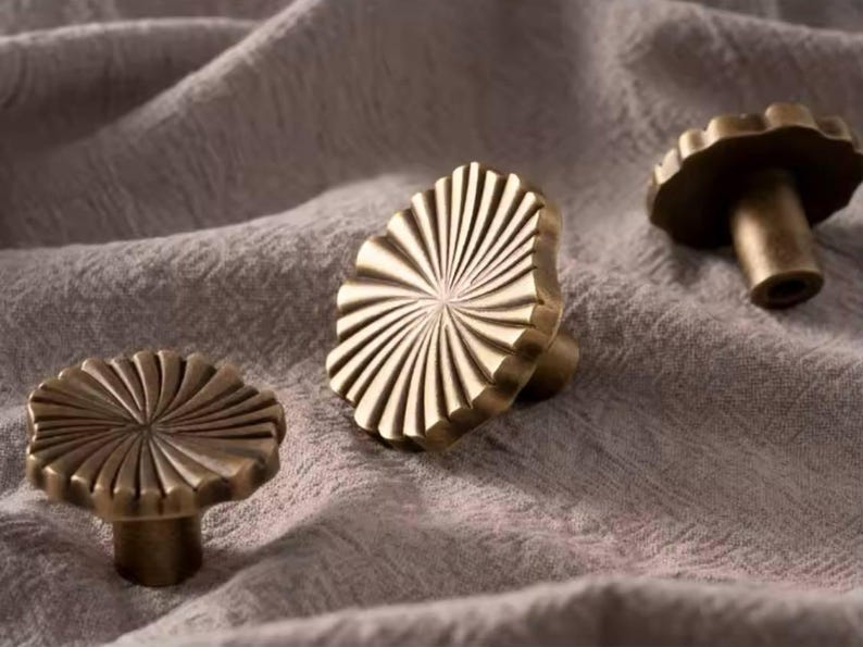 May include: Three gold-toned cabinet knobs with a sunburst design. The knobs are made of metal and have a smooth, polished finish.