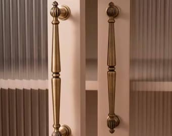 May include: Two antique gold cabinet door pulls with ornate details. The pulls are attached to a light pink cabinet door with a frosted glass panel.