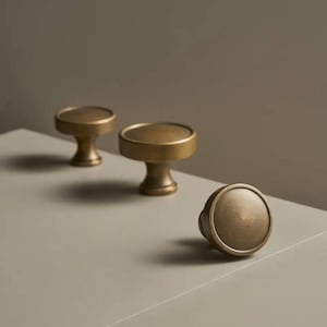 May include: Three antique brass cabinet knobs with a round, slightly domed top and a short, cylindrical base.