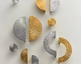 May include: Assortment of gold and silver half-circle cabinet knobs with a textured, sunburst design. The knobs are arranged in a random pattern on a white background.