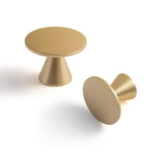 Op de afbeelding: Twee goudkleurige kastknoppen. Elke knop heeft een cirkelvormige bovenkant en een conische basis. De knoppen zijn gemaakt van metaal en hebben een gladde, matte afwerking. Eén knop staat rechtop, de andere ligt op zijn kant.