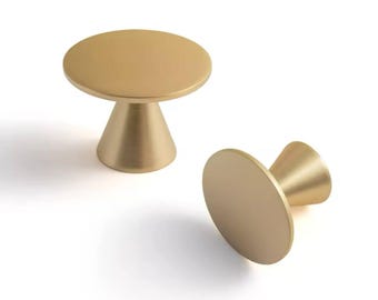 May include: Two gold-colored cabinet knobs. Each knob features a circular top and a conical base. The knobs are made of metal and have a smooth, matte finish. One knob is upright, while the other is lying on its side.