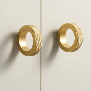 以下が含まれることがあります： 円形のデザインとテクスチャ加工された表面を持つ、金色のキャビネットノブが2つあります