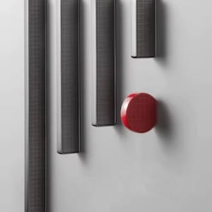 May include: A set of contemporary speakers and a red control button are mounted on a light grey wall. The speakers are rectangular with a dark grey mesh design and silver trim. The button is a solid red colour.