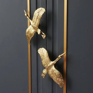 Puede incluir: Dos tiradores de puerta en forma de grúa de color dorado montados en una puerta azul oscuro con moldura dorada.