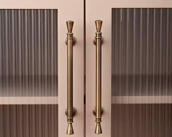 May include: Two antique gold cabinet door pulls with a fluted design. The pulls are attached to a cabinet with glass doors.