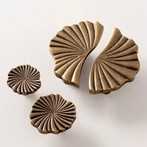 May include: Set of three antique gold cabinet knobs with a fan-shaped design. The largest knob is split into two pieces.