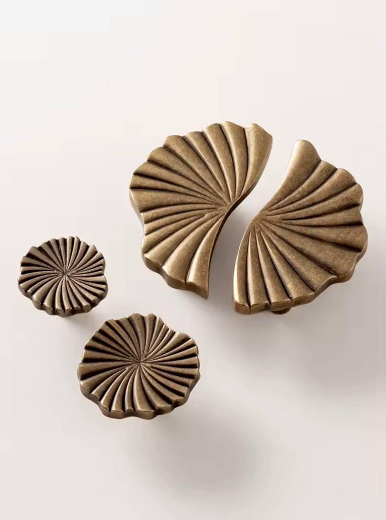 May include: Set of three antique gold cabinet knobs with a fan-shaped design. The largest knob is split into two pieces.