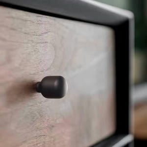 Op de afbeelding: Een close-up van een houten lade met een zwart metalen frame en een donkergrijze metalen knop.