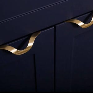 Op de afbeelding: Twee donkerblauwe kastdeuren met gouden metalen handgrepen. De handgrepen zijn gebogen en hebben een modern ontwerp.