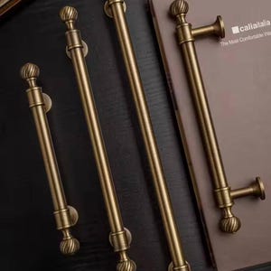 May include: Four antique brass door handles with a decorative ball finial design. The handles are in varying lengths and are mounted on a dark surface. The image also shows a book with the text "caliaitalia" and "The Most Comfortable Way".
