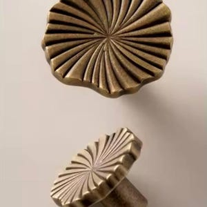 May include: Two antique brass cabinet knobs with a sunburst design. The top knob is flat and the bottom knob has a post.