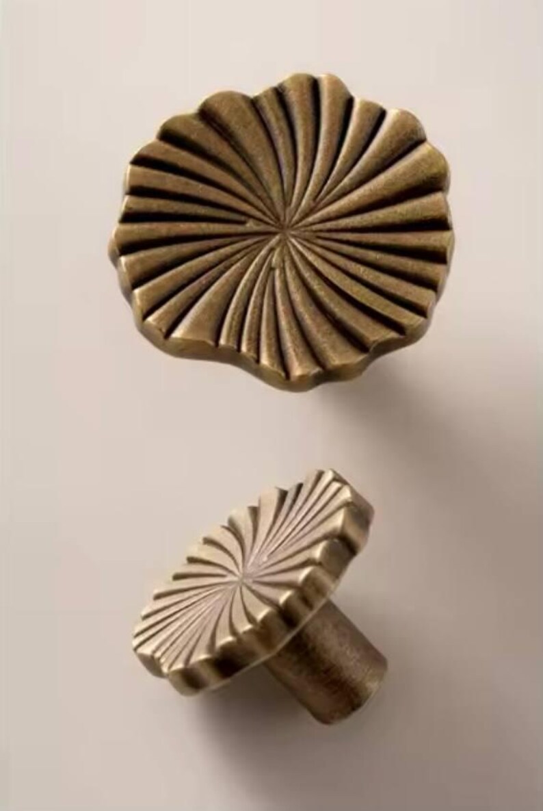 May include: Two antique brass cabinet knobs with a sunburst design. The top knob is flat and the bottom knob has a post.