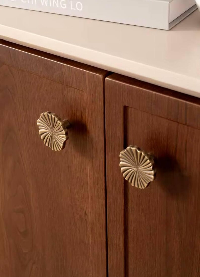 May include: Two wooden cabinet doors with brass flower-shaped knobs. The cabinet doors are a dark brown wood.