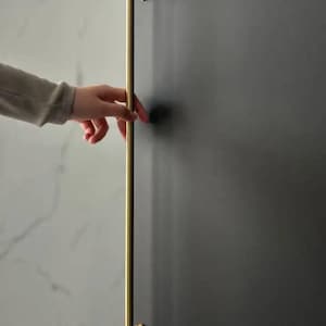 May include: A gold-toned metal door handle with a vertical design. The handle is attached to a wall with two round, decorative plates.