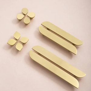 May include: Two brass cabinet pulls with a split design and rounded ends.  There are also four smaller brass cabinet pulls in the shape of a flower with four petals.