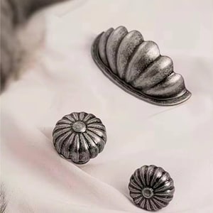 May include: Three silver-toned cabinet knobs with a decorative, fluted design. The knobs are in the shape of a flower and a half-circle.