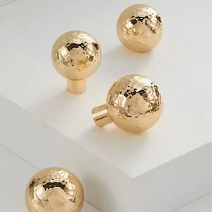 May include: Four gold hammered metal knobs with a round shape. The knobs have a textured surface and are perfect for adding a touch of modern style to any home.