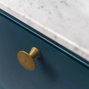 Könnte beinhalten: Nahaufnahme eines Messing-Schrankknaufs mit runder, strukturierter Basis und einem leicht konischen Stiel. Der Knauf ist an einer dunkelblauen Schranktür montiert.