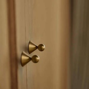 May include: Two gold-toned door knobs with a rounded, cone-shaped design. The knobs are mounted on a wooden door.