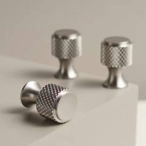 May include: Three silver metal cabinet knobs with a textured, diamond-shaped pattern. The knobs have a round, flat top.