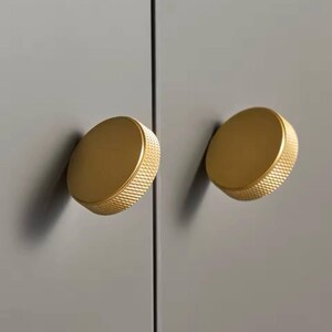 Peut inclure: Deux boutons ronds en or pour armoire avec une surface texturée.