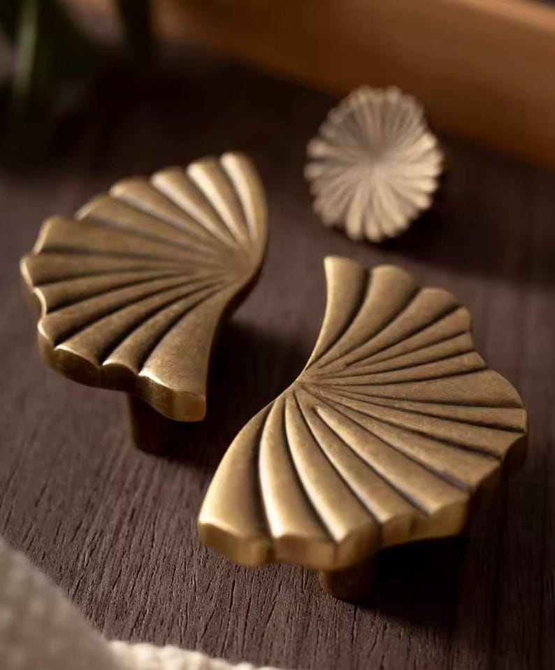 May include: Two gold-toned metal cabinet pulls shaped like a fan with a scalloped edge.