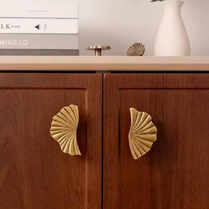 May include: Two wooden cabinet doors with brass leaf-shaped handles. The cabinet doors are a rich brown colour and the handles are a shiny gold.
