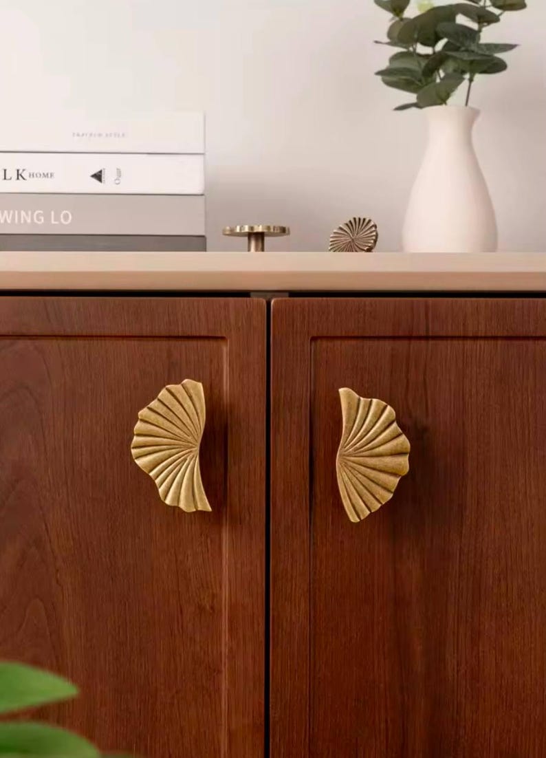 May include: Two wooden cabinet doors with brass leaf-shaped handles. The cabinet doors are a rich brown colour and the handles are a shiny gold.