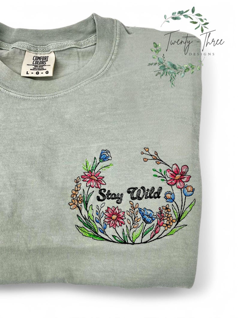 May include: A light green t-shirt with a floral design and the text "Stay Wild" in black.