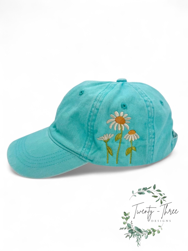May include: A turquoise blue baseball cap with embroidered white daisies. The daisies have yellow centers.