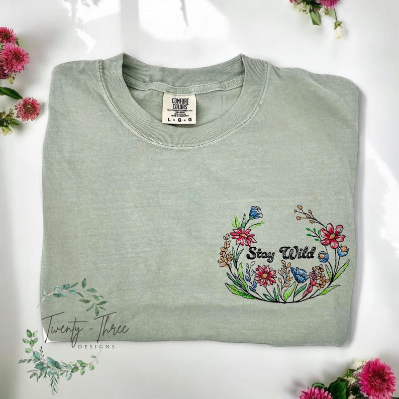 May include: Sage green t-shirt with an embroidered floral wreath and the text "Stay Wild".