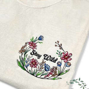 May include: A white t-shirt with an embroidered floral wreath design that says "Stay Wild".