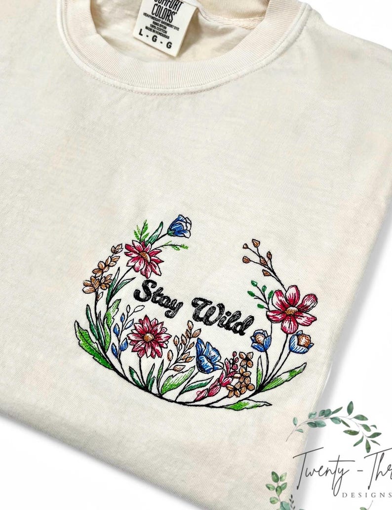 May include: A white t-shirt with an embroidered floral wreath design that says "Stay Wild".